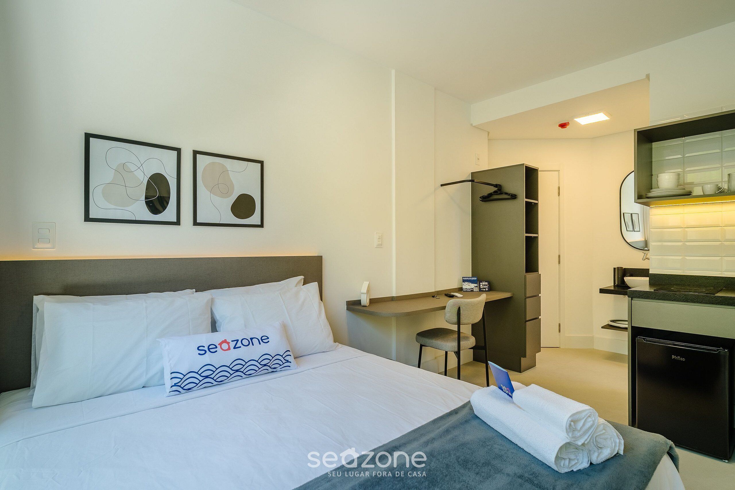 Habitación de hotel con cama, escritorio, silla, refrigerador pequeño y baño.