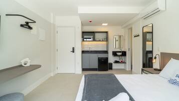 Habitación de hotel con cama, escritorio, silla, kitchenette pequeña y baño.