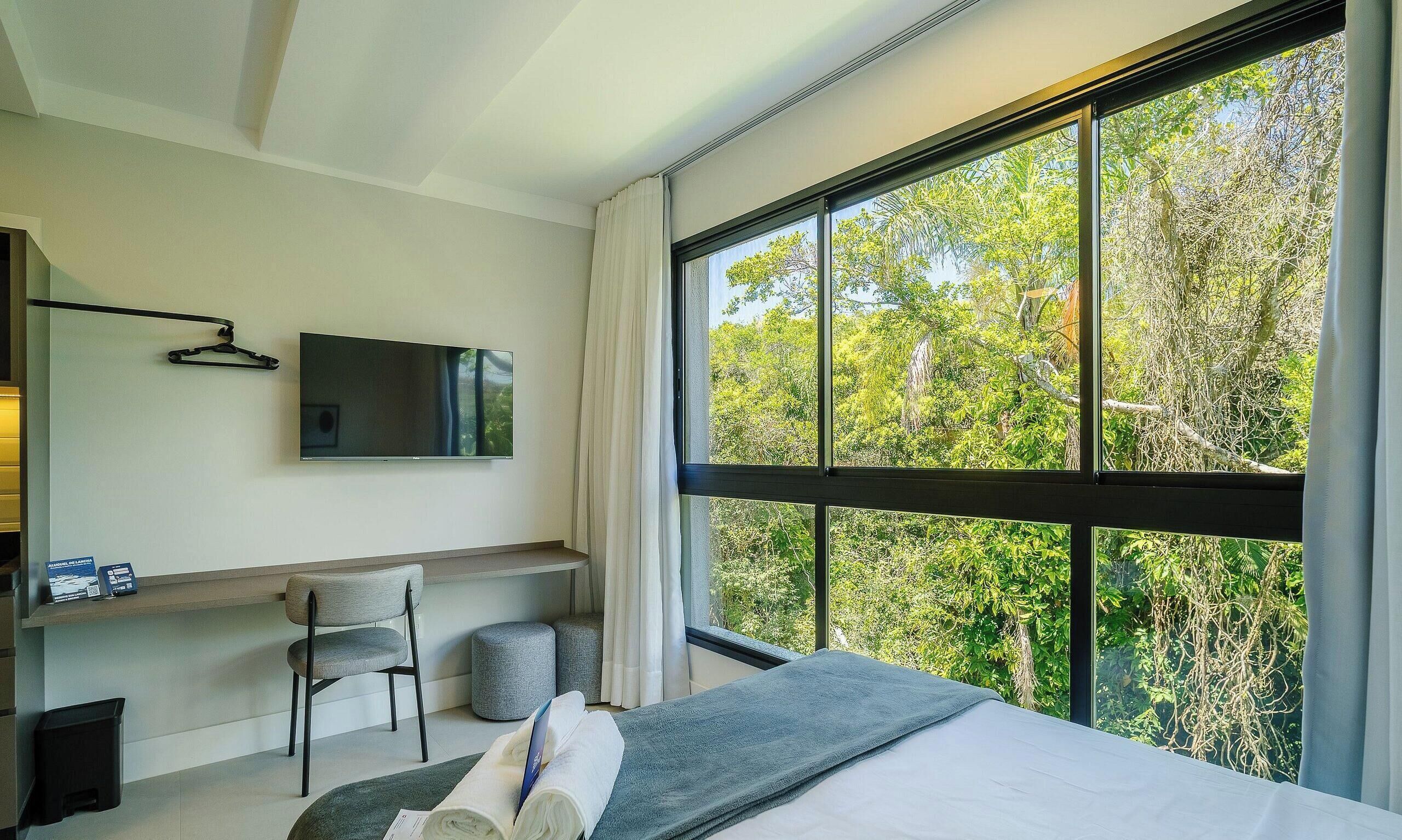 Una habitación de hotel moderna con un ventanal grande, un televisor de pantalla plana, un escritorio, una silla y una cama.