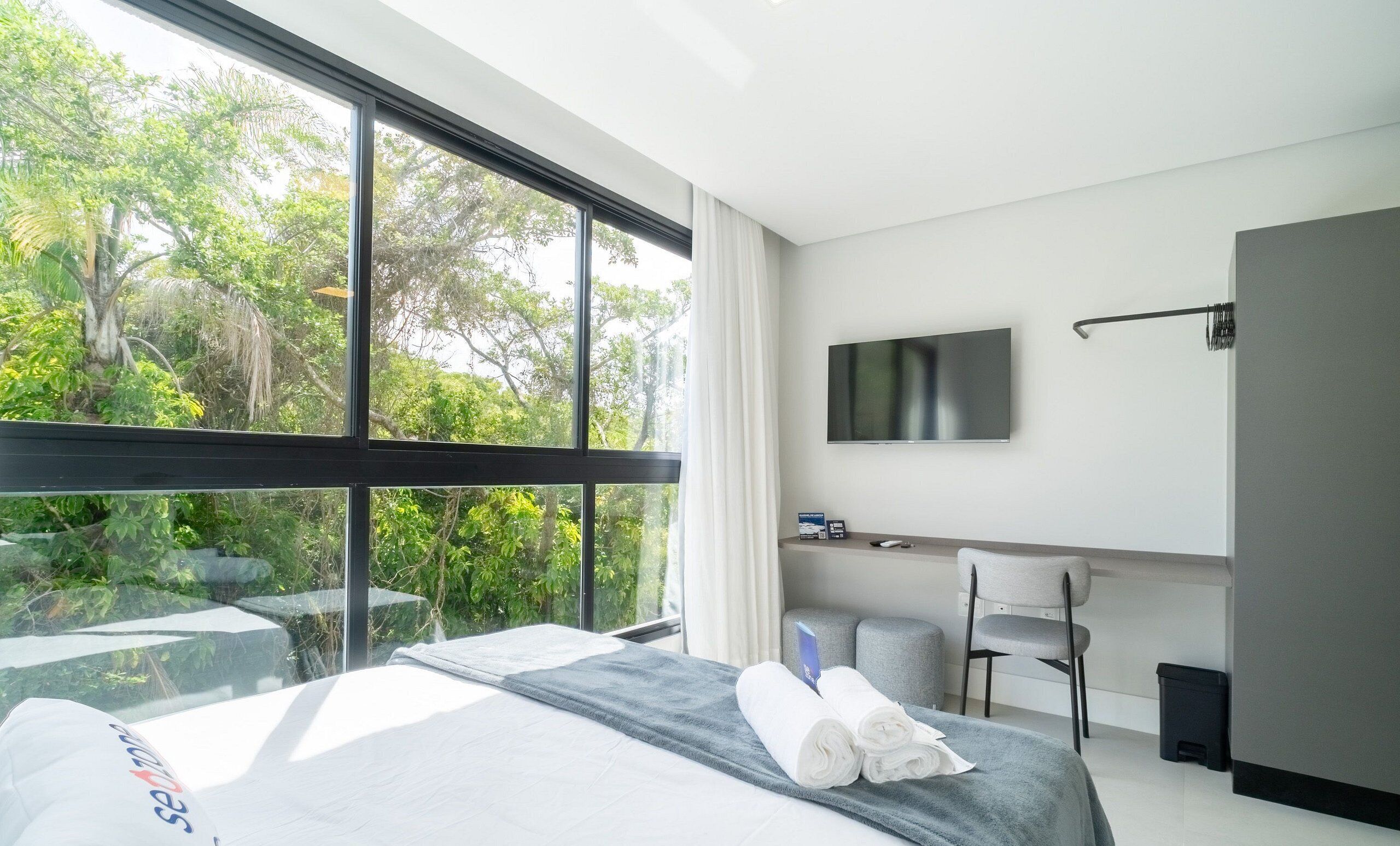 Habitación de hotel con cama, escritorio, silla, televisor y vistas a la vegetación.