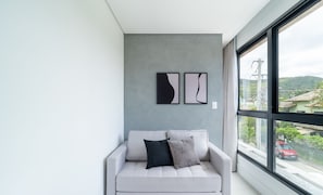 Una sala de estar moderna con un sofá gris, dos obras de arte abstracto en la pared y un ventanal con vistas a un paisaje urbano.