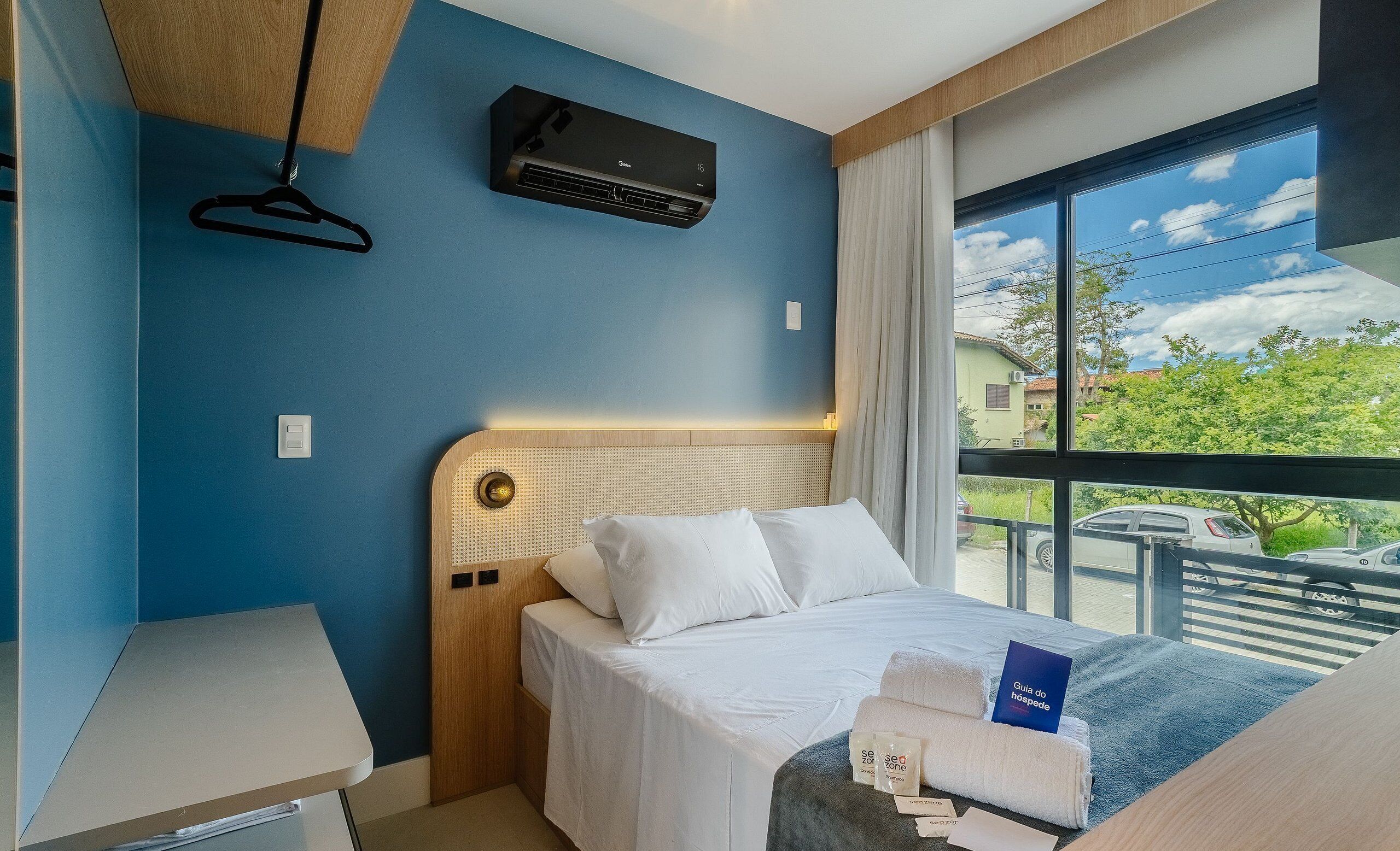 Habitación de hotel con cama, escritorio, lámpara colgante, ventana con vistas y aire acondicionado.
