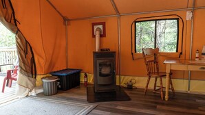 Ein Zeltraum mit Holzofen, einem Stuhl, einem Tisch und einem Fenster.