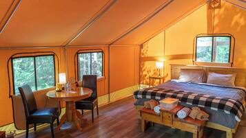A tented accommodation with a bed, a table, chairs, and a bench.