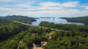 Luftaufnahme eines bewaldeten Gebietes mit einer Brücke, einem See und einer kleinen Siedlung mit Häusern und parkenden Autos.