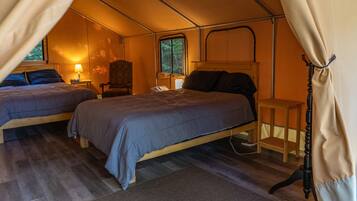 A tented accommodation with two beds, a chair, and a bedside table.