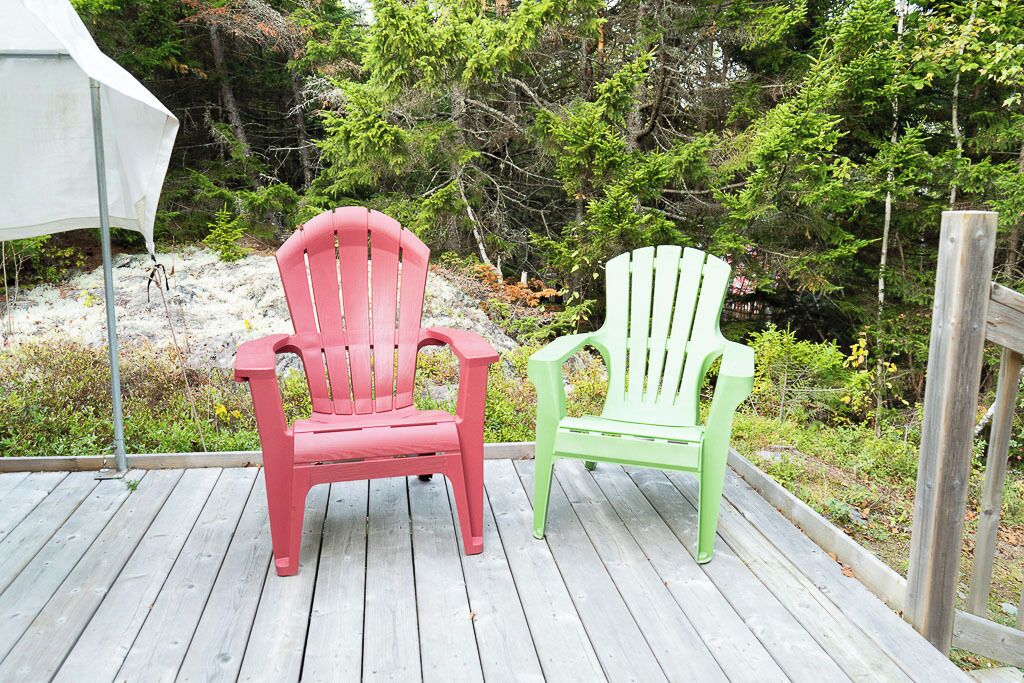 Due poltrone Adirondack su un pontile di legno, con una foresta sullo sfondo.