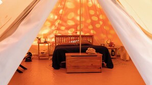 A cozy tent with a bed, a wooden chest, a small table with a lamp, and a mirror.
