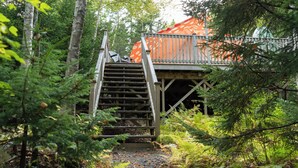 Un escalier en bois mène à un chalet rustique à toit rouge, entouré d’une forêt dense.