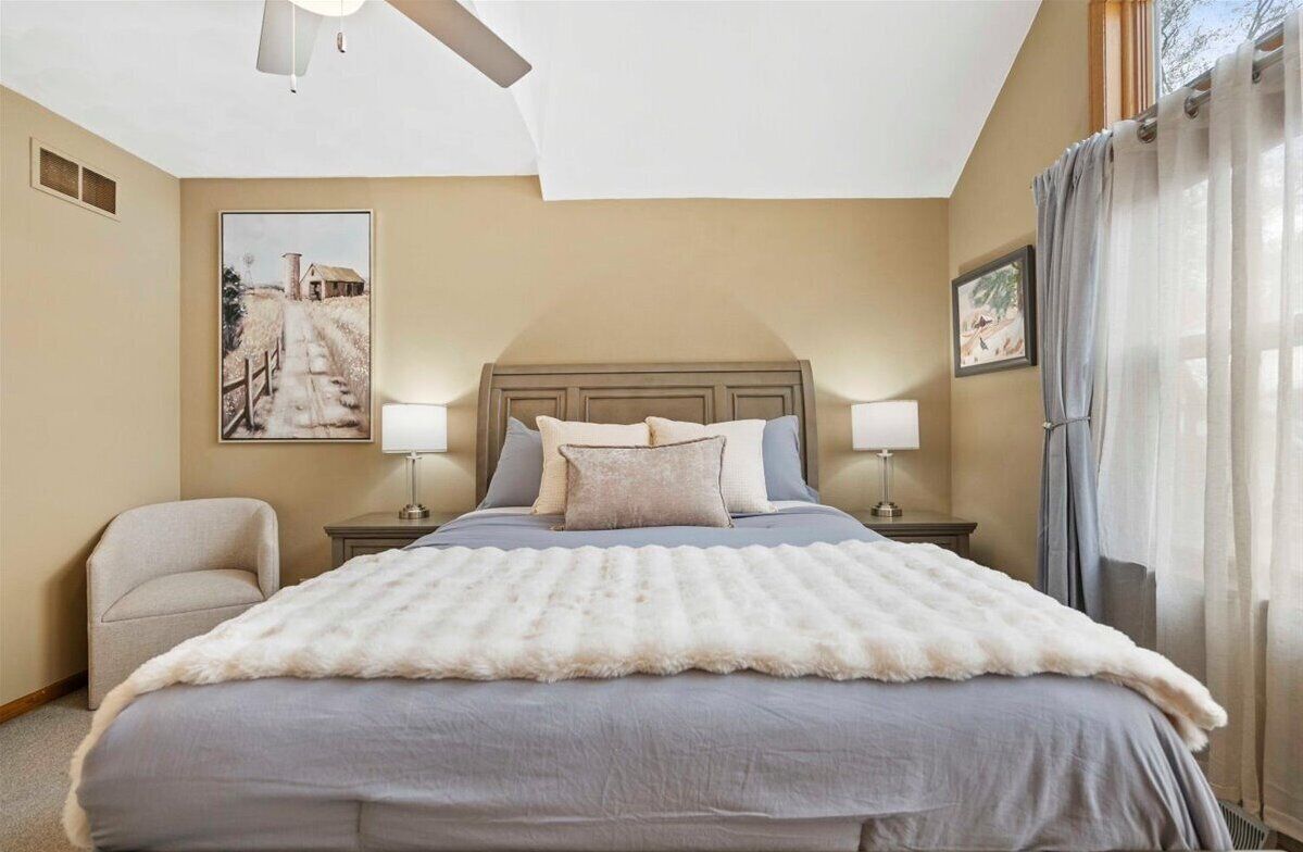 A bedroom with a large bed, two bedside tables, a chair, and a ceiling fan.
