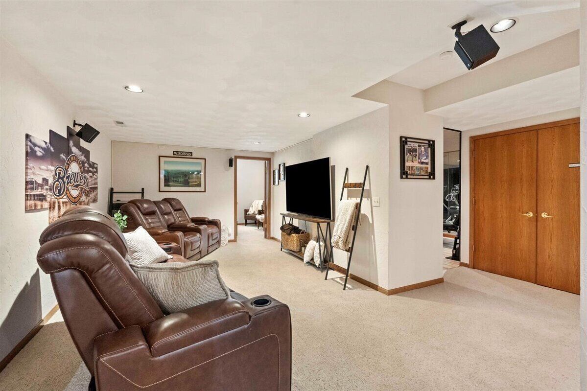 A living room with a brown leather sofa, a flat-screen TV, a painting on easel, and a wooden door.