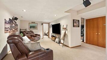 A living room with a brown leather sofa, a flat-screen TV, a painting on easel, and a wooden door.