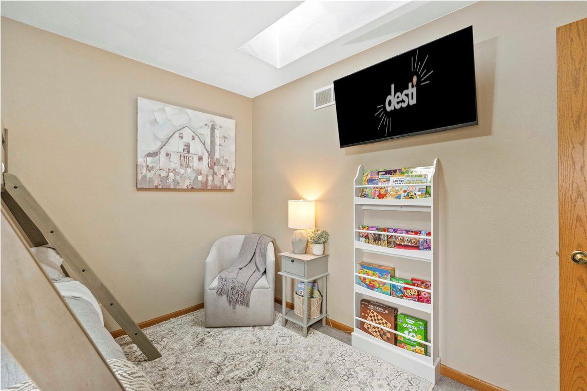 Una habitación con cama, una silla, una estantería, un cuadro y un televisor.