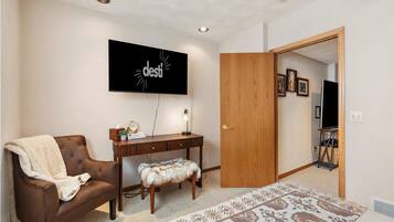 Una sala de estar con un sofá de cuero marrón, un escritorio de madera, un tapete estampado y un televisor montado en la pared.