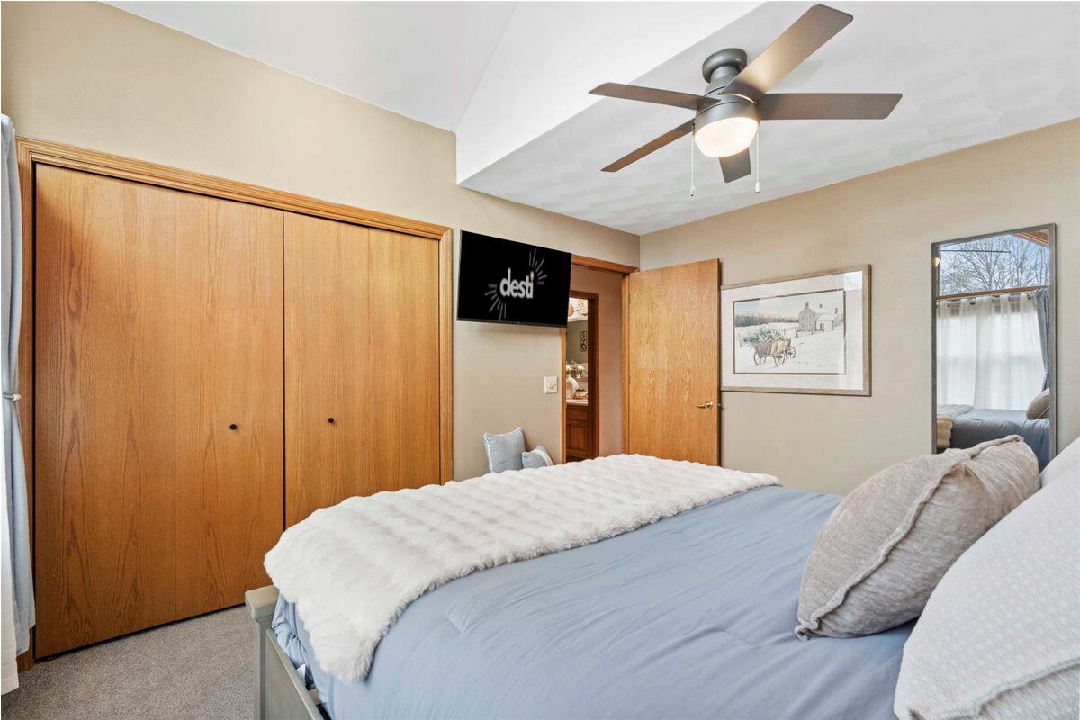 Quarto com cama, ventoinha no teto, guarda-roupa de madeira, quadro emoldurado e janela com cortinas.