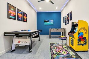 Una stanza con un tavolo da calcio, un tavolo da biliardo e una macchina arcade Pac-Man.