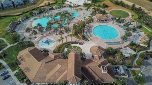 Vista aerea di un resort con diverse piscine, palme e un edificio centrale con tetto in tegole.