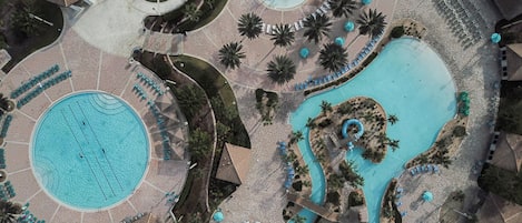 An aerial view of a resort with a large central pool, a smaller circular pool, and a water slide.