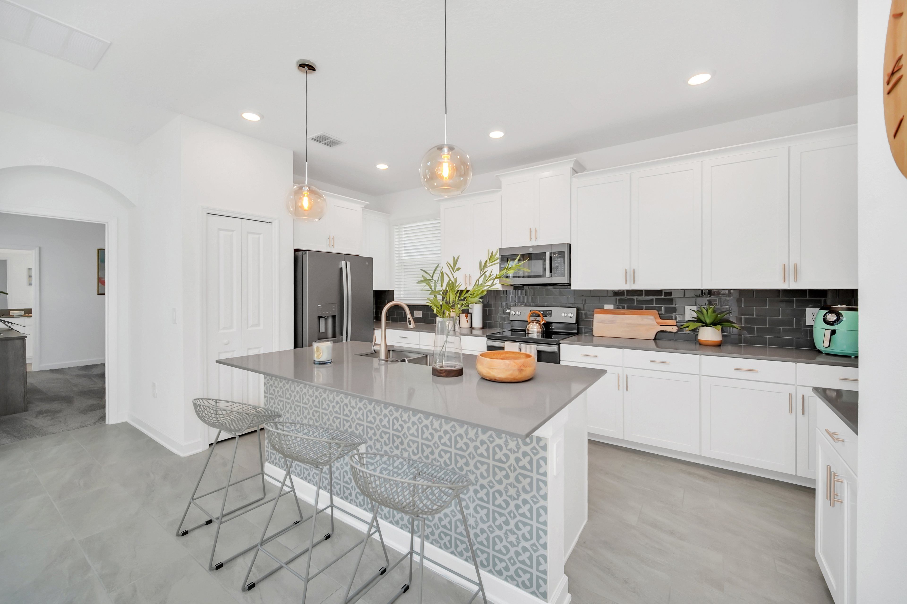 A modern kitchen with white cabinets, a central island, bar stools, pendant lighting, and a microwave.