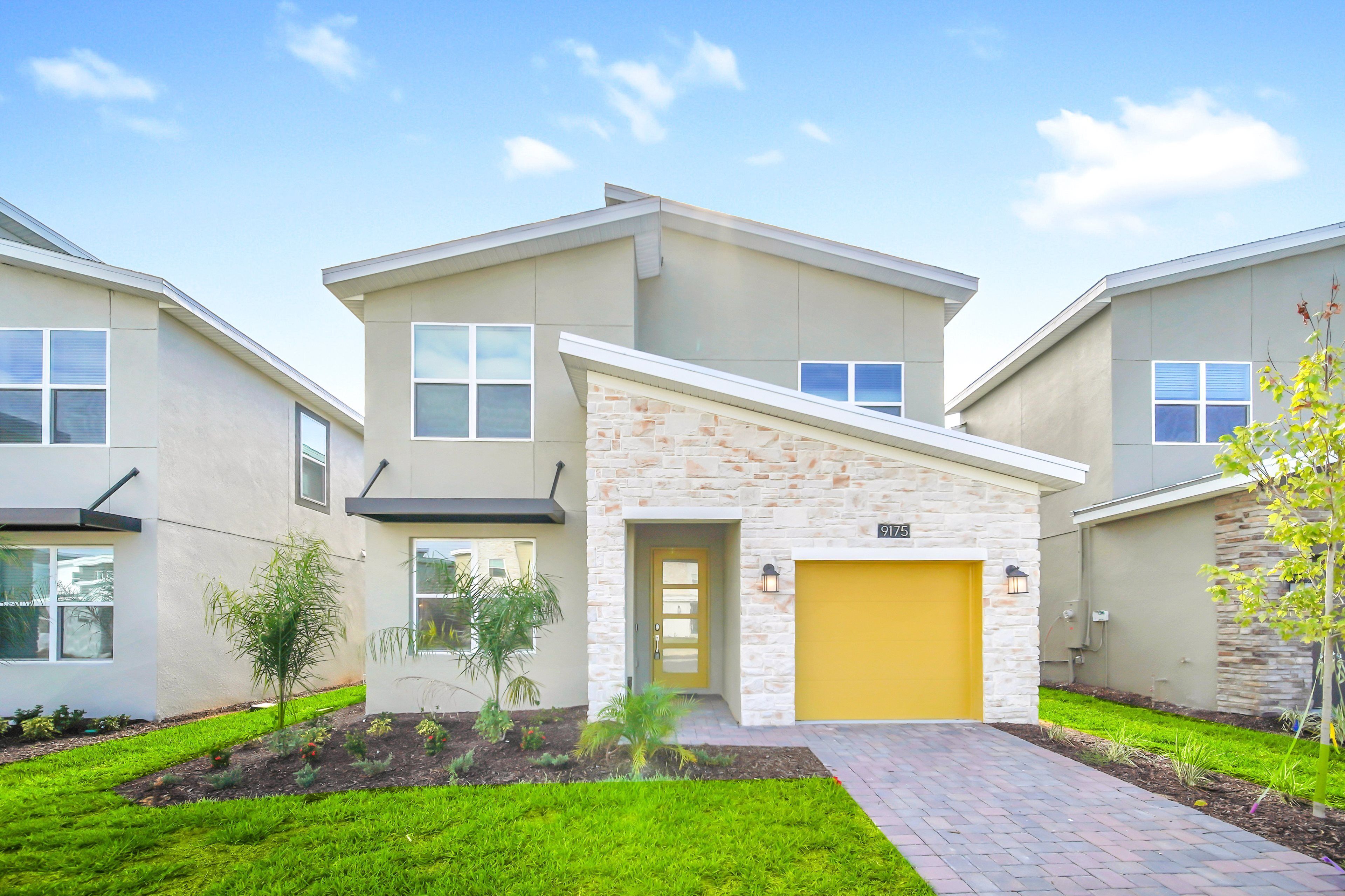 A modern two-story house with a stone facade, a yellow garage door, and a well-maintained lawn.