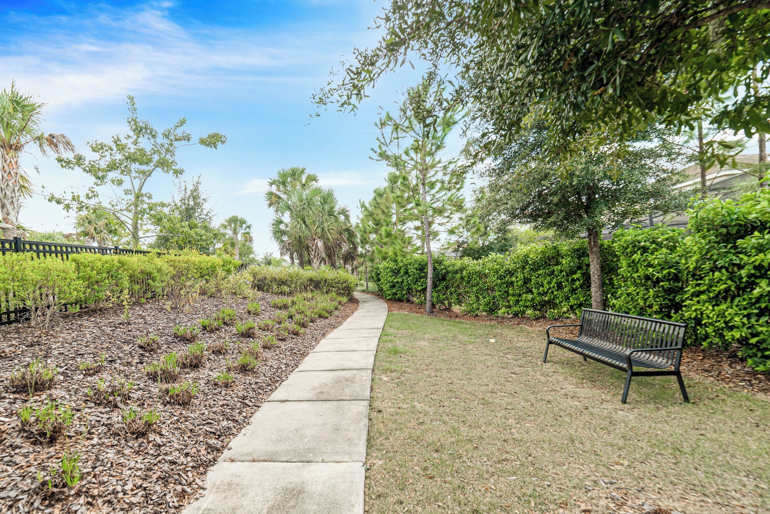 A paved pathway leading through a landscaped area with a bench on the right.