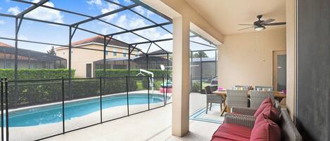 Un espace extérieur abrité comprenant une piscine, des meubles en osier et un ventilateur de plafond.