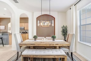 Un comedor con mesa de madera, sillas acolchadas, un banco y una lámpara colgante.