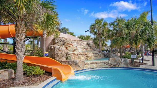 A pool area with a water slide, palm trees, and a rocky waterfall backdrop. - Family Paradise - Theatre + Resort + Pet Friendly (Davenport)