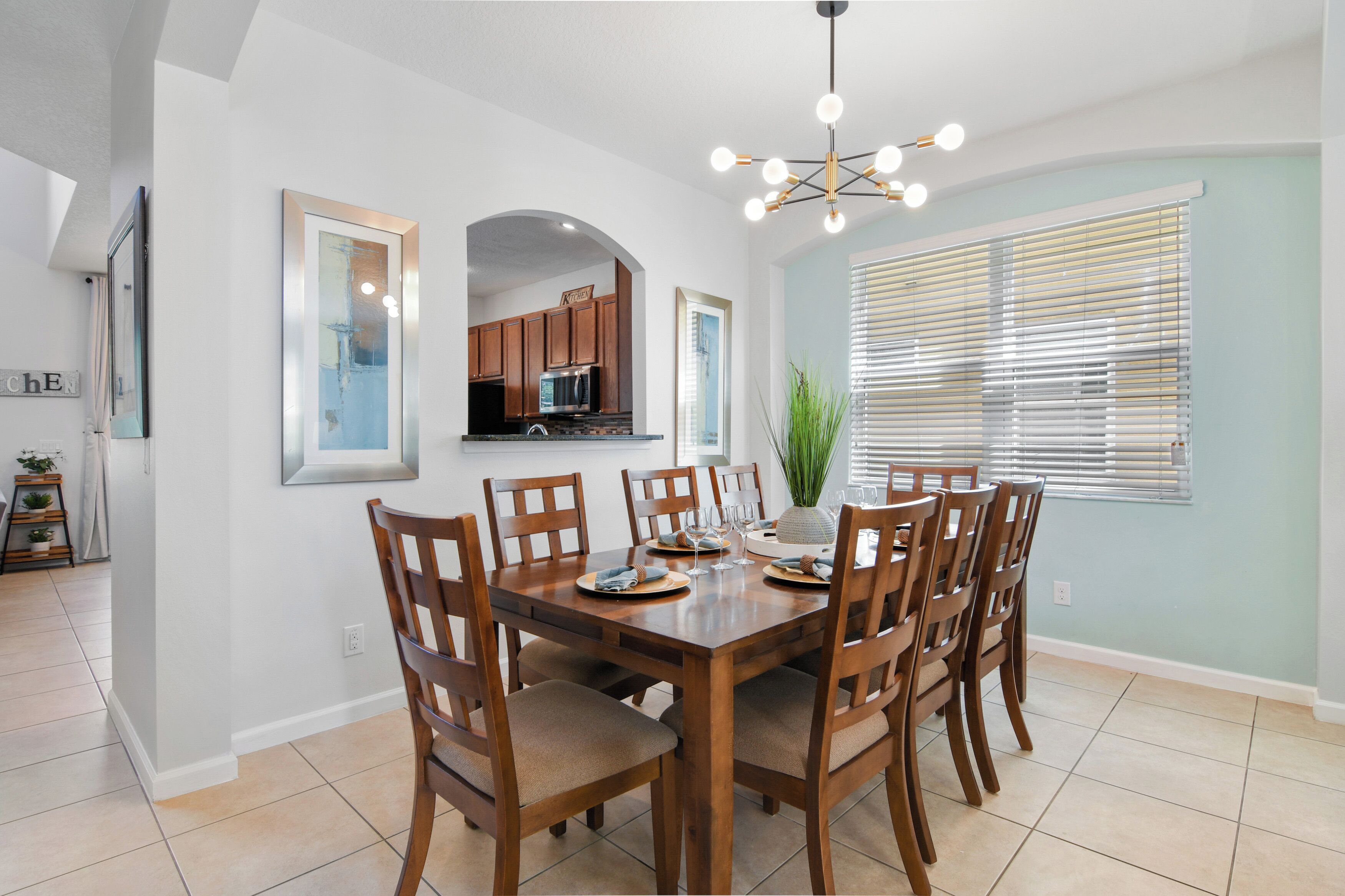 A dining area with a wooden table and chairs, a chandelier, and a view of the kitchen through an archway.