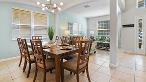 A dining area with a wooden table and chairs, a chandelier, and a view into a living room with a sofa and a 'WELCOME' sign. - Family Paradise - Theatre + Resort + Pet Friendly (Davenport)