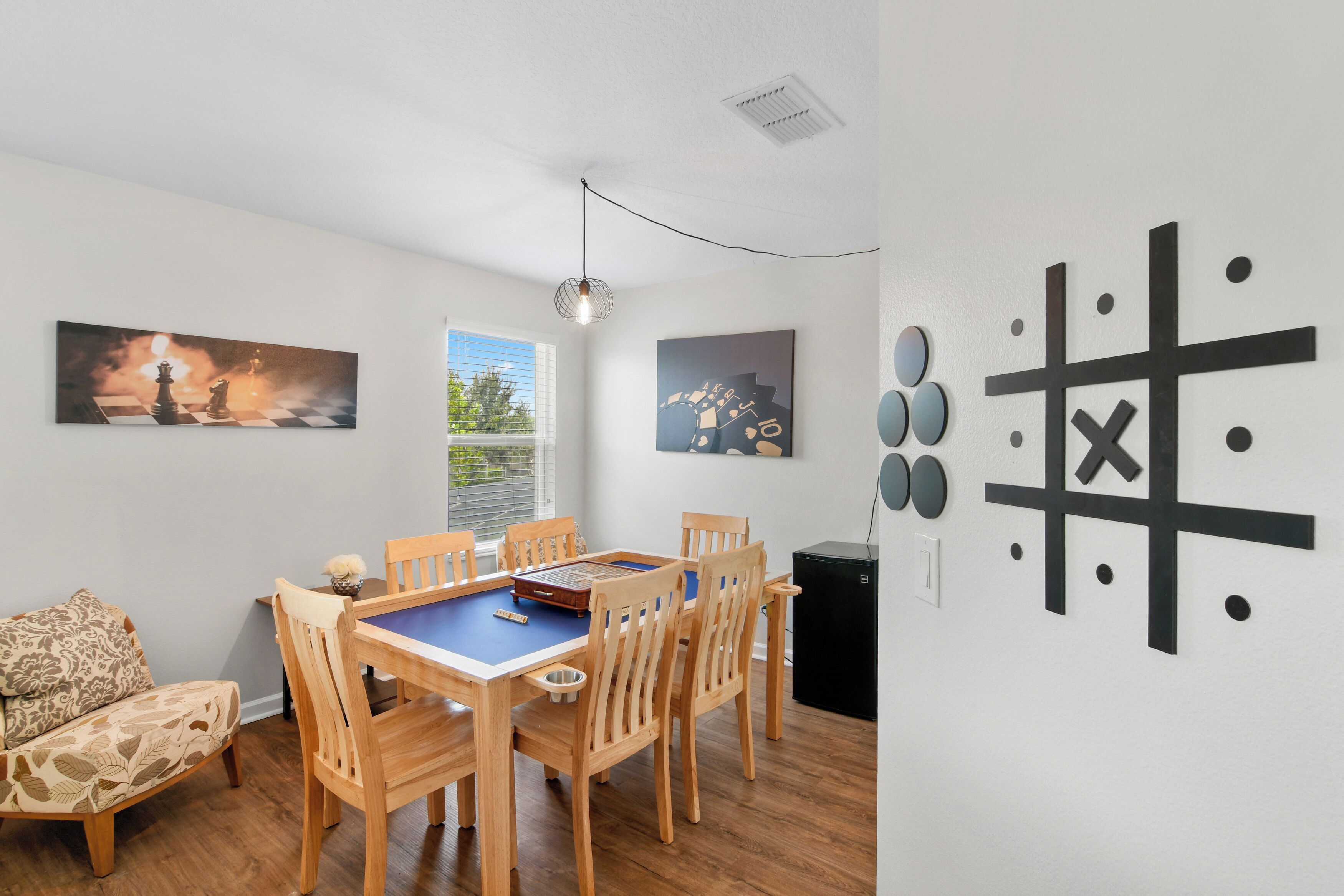 A dining area with a wooden table and chairs, a chessboard, and two wall-mounted artworks.