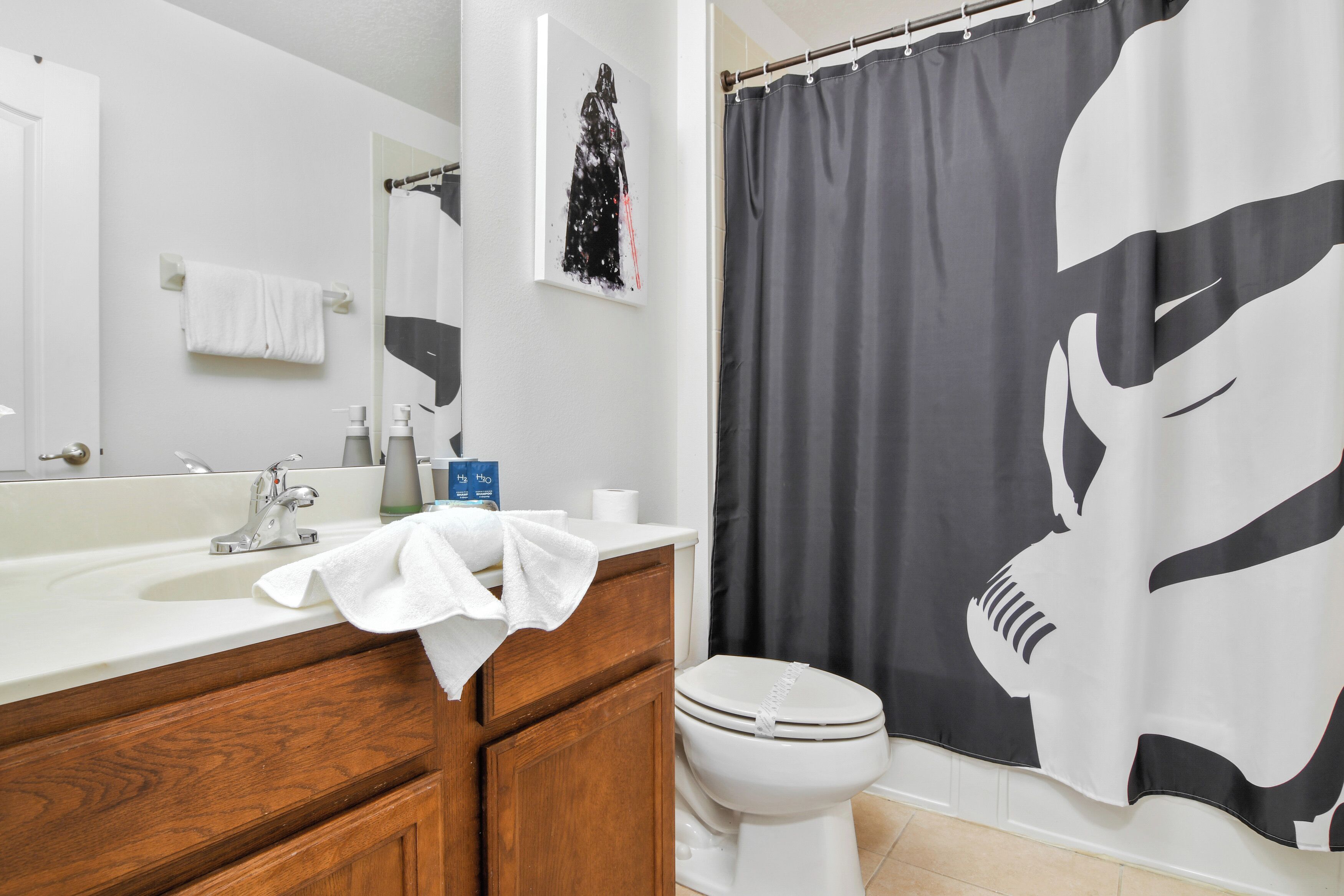 Ein Badezimmer mit einem weißen Waschbecken, Holzschränken, einer Toilette und einem Duschvorhang mit großem Schwarz-Weiß-Muster.
