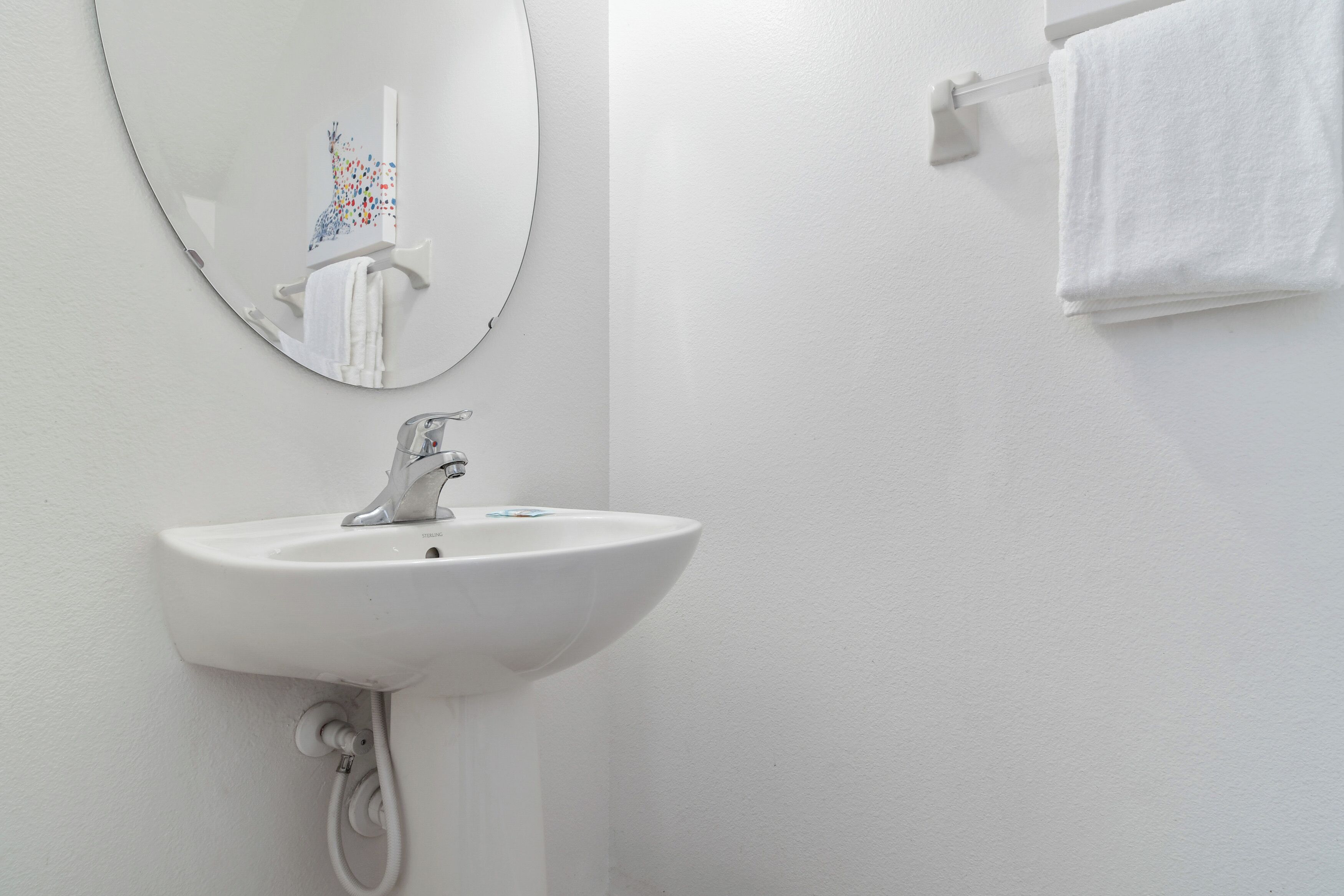 Un baño con lavamanos blanco, espejo y toallero.