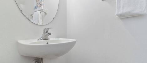 Un baño con lavamanos blanco, espejo y toallero.