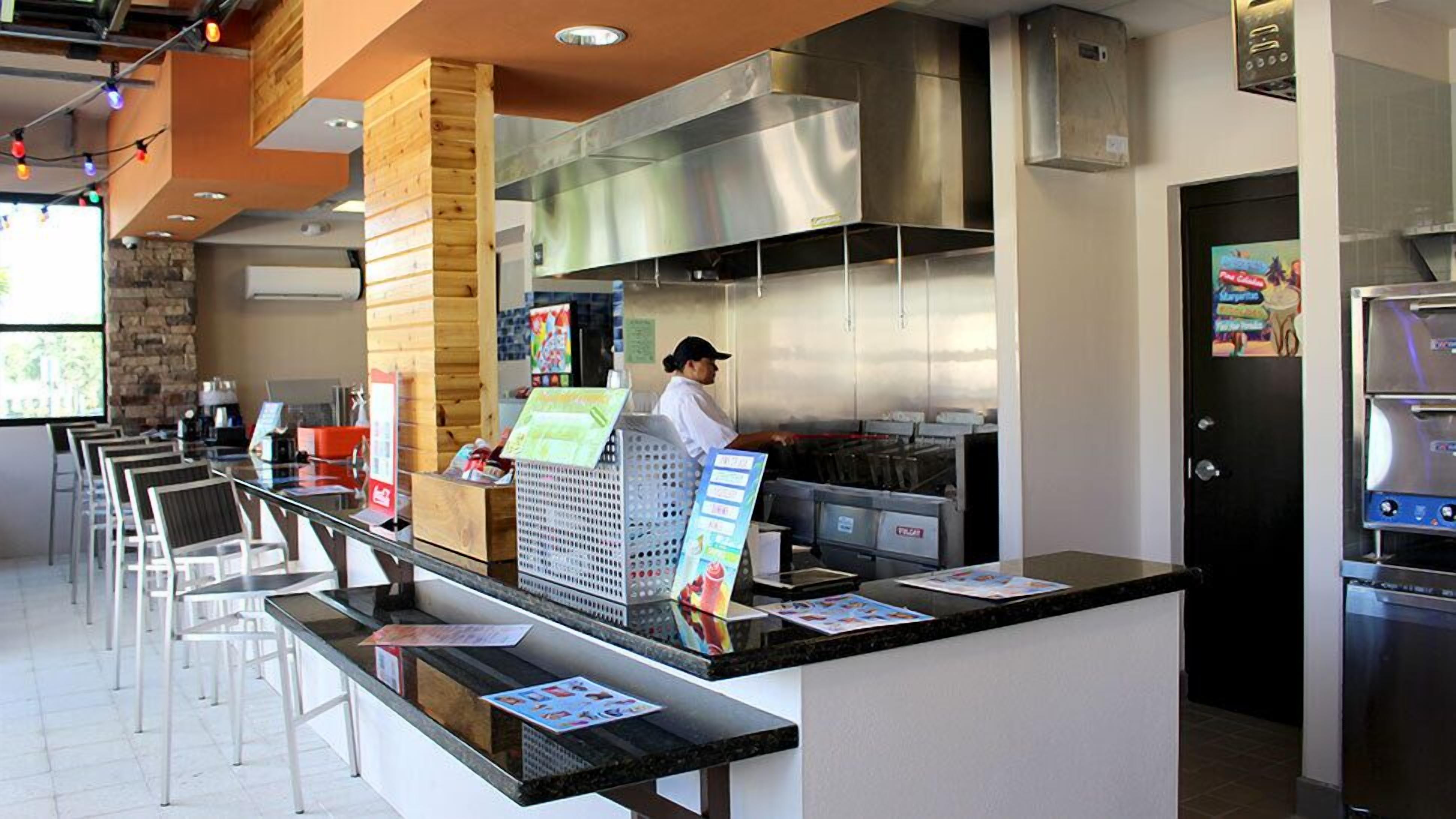 A restaurant with a counter, chairs, and a kitchen area.