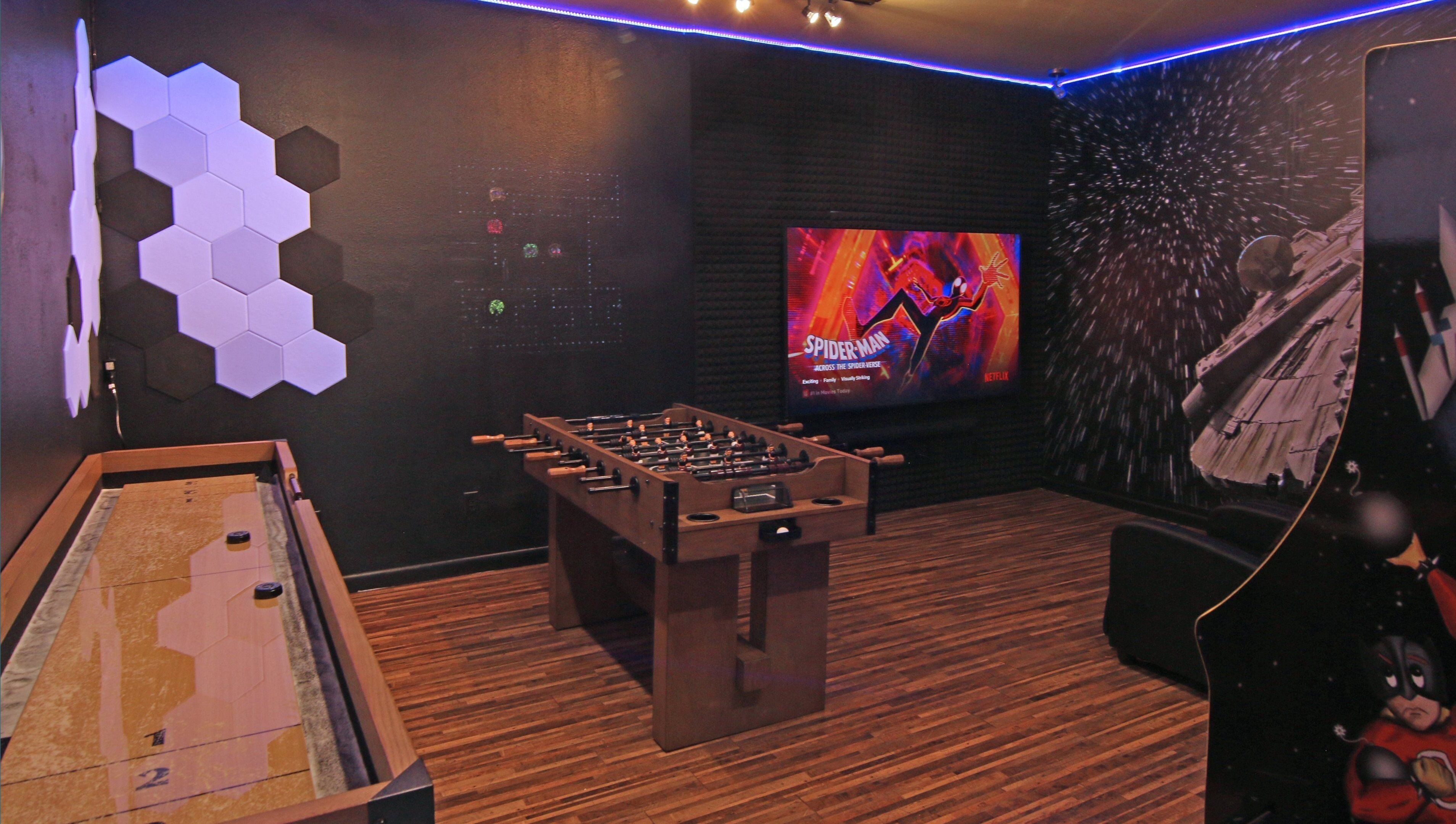 A room with a foosball table, a large screen displaying a movie, and hexagonal wall decorations.