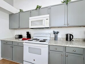 A kitchen with grey cabinets, a white stove, a microwave, a toaster, and a kettle. - Serene Escape: South-facing Pool & Game Room (Clermont)