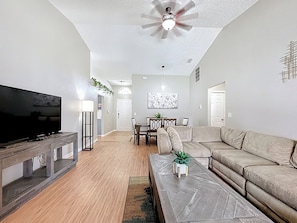 A living room with a television, sofa, coffee table, and ceiling fan. - Serene Escape: South-facing Pool & Game Room (Clermont)