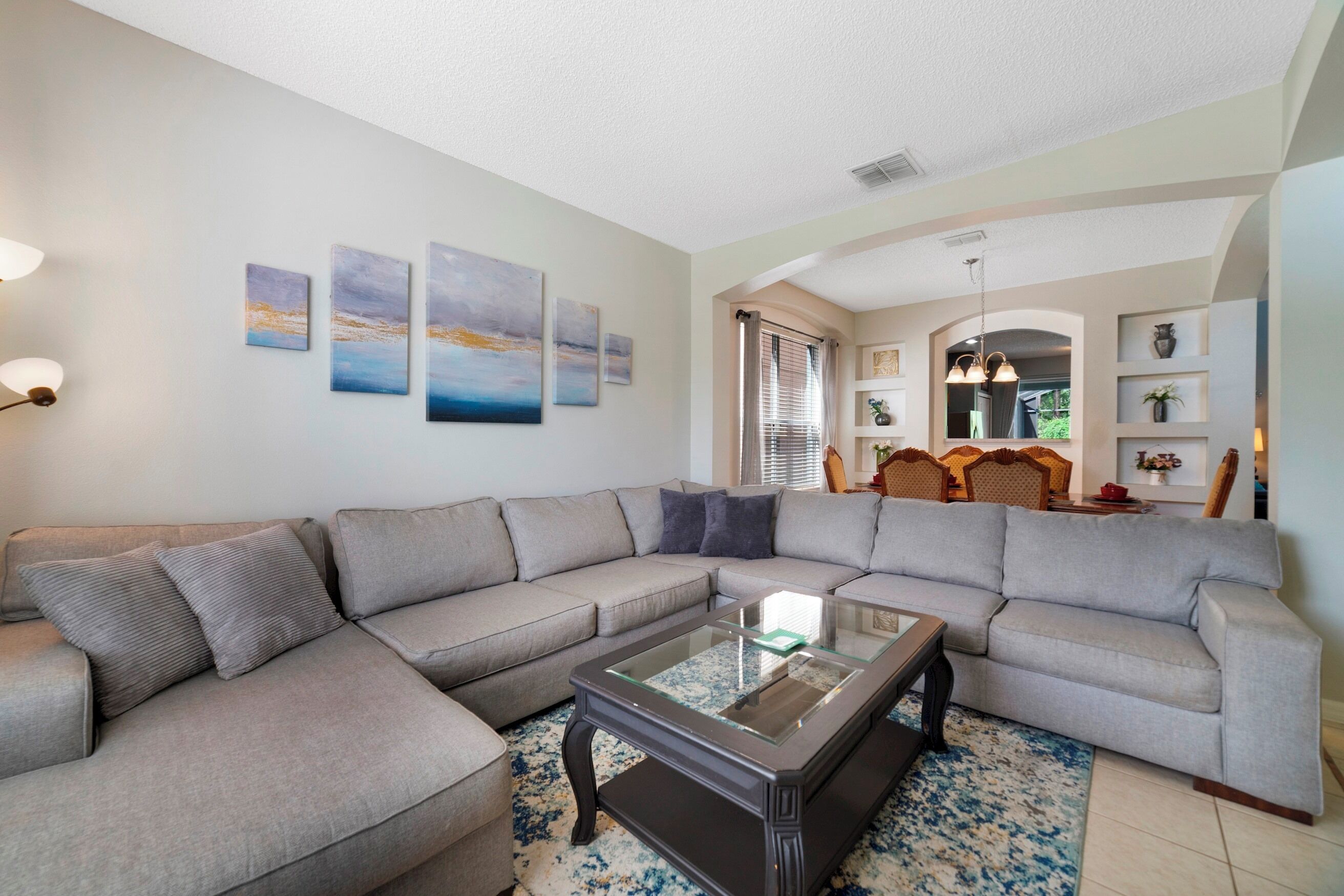 A living room with a sectional sofa, a glass coffee table, and artwork on the wall.