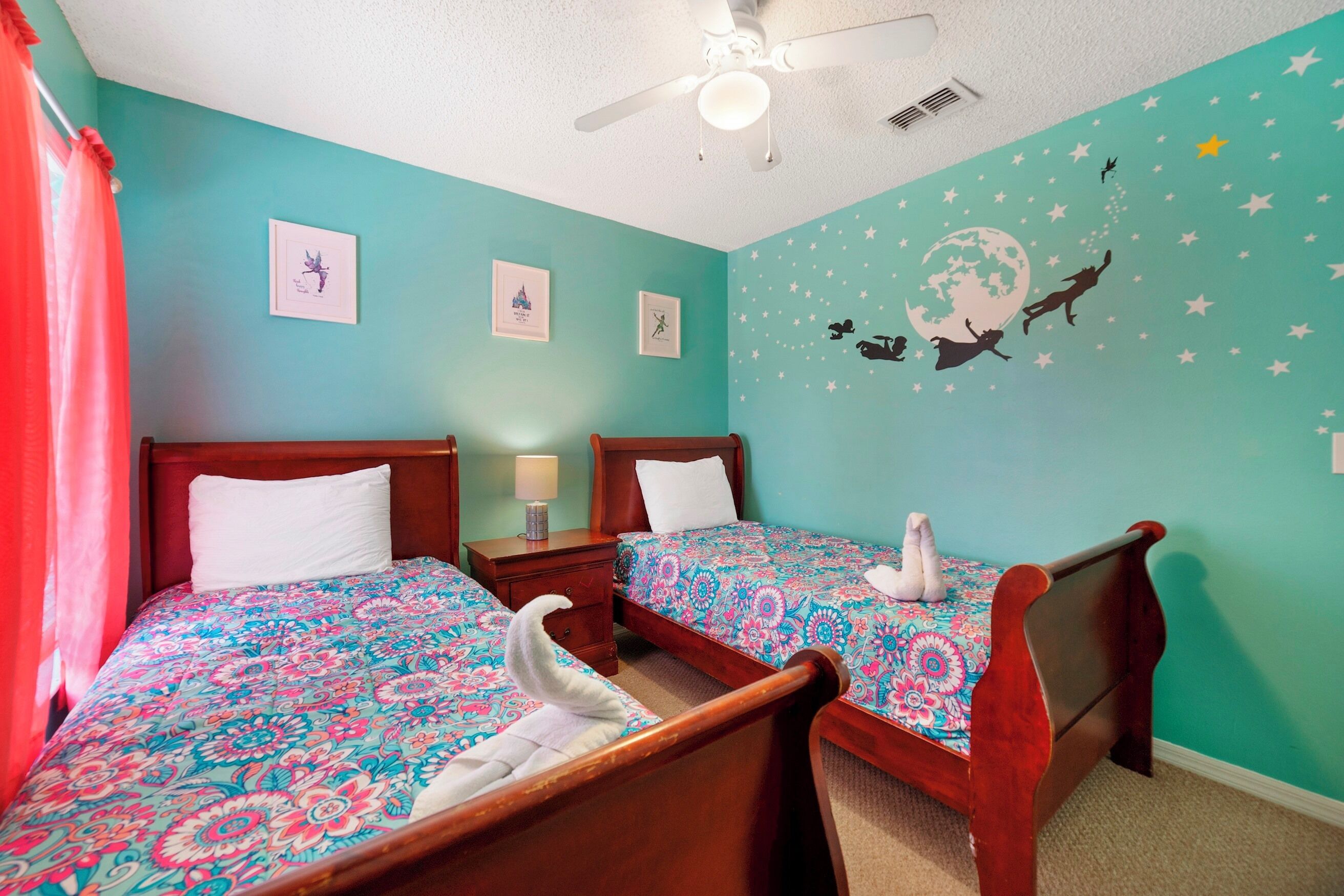 A room with two wooden beds, a ceiling fan, and a wall with a starry night mural.