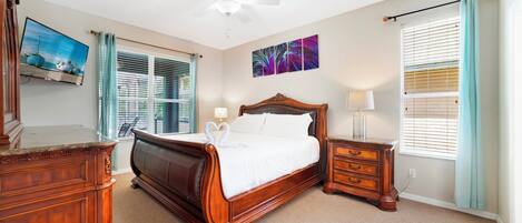 A bedroom with a wooden bed, a ceiling fan, a TV, and a window with blinds.