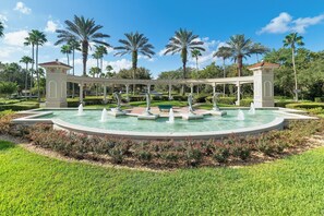 A fountain with multiple water jets, surrounded by a well-manicured lawn and palm trees. - Magical Paradise - Resort Home & In-door Arcade (Kissimmee)