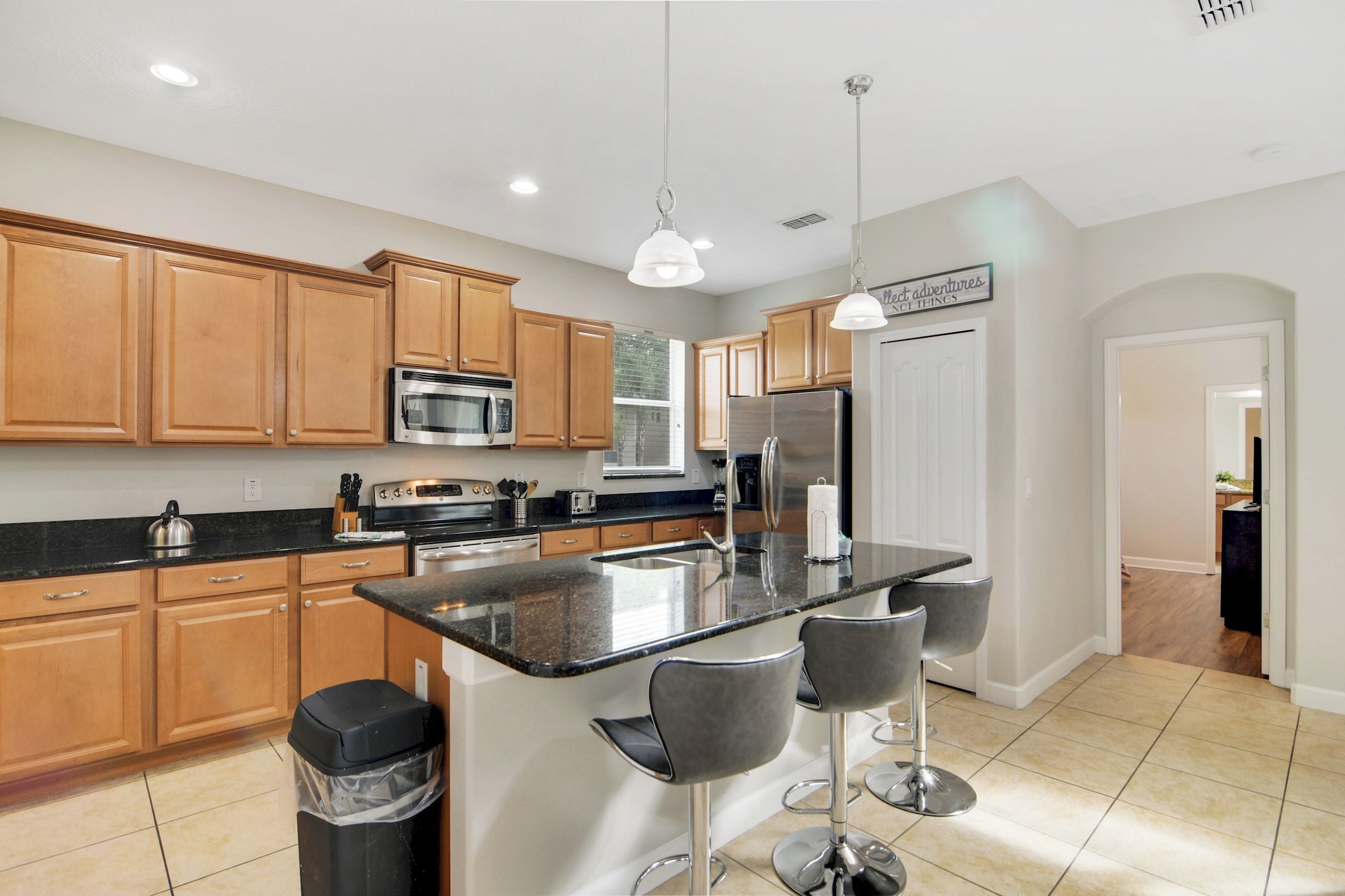 A modern kitchen with wooden cabinets, stainless steel appliances, a central island with bar stools, and pendant lighting.