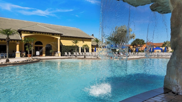 A swimming pool with a water feature, a building with a tiled roof, and palm trees. - Villa Paradiso - South-facing Pool + Luxe Resort! (Kissimmee)