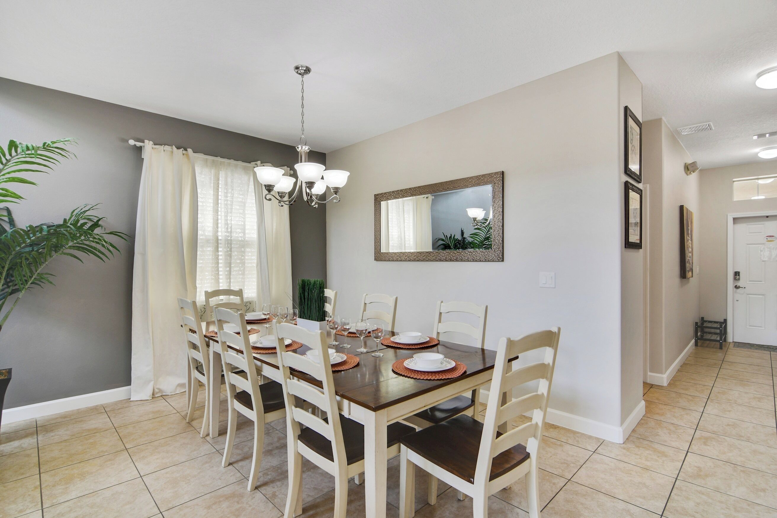 A dining area with a table set for six, a chandelier, and a mirror on the wall.