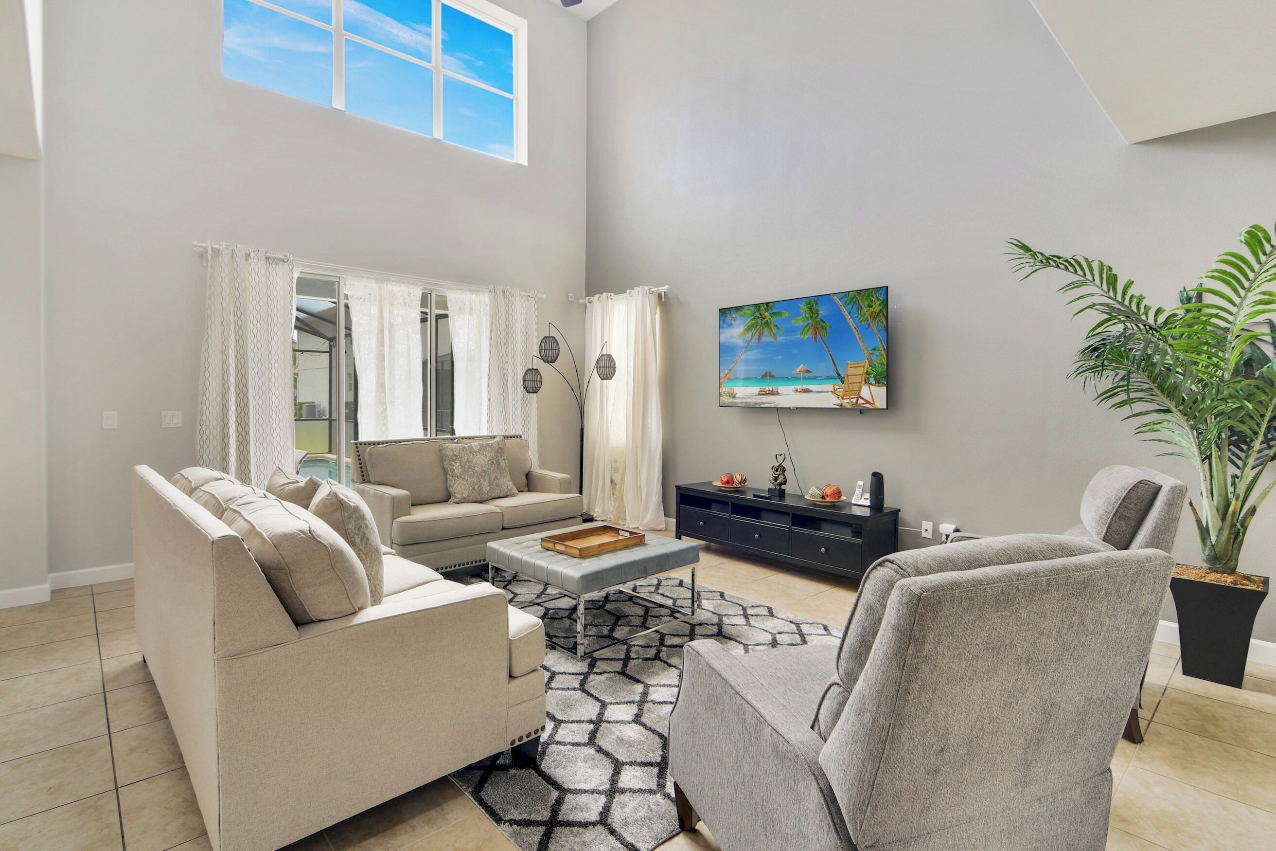 A living room with a sofa, armchairs, a coffee table, a TV, a painting, and a potted plant.