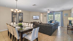 A spacious living area with a dining table, chairs, a sofa, and a TV. - Tranquil Terrace - 10 Mins to Disney! (Kissimmee)