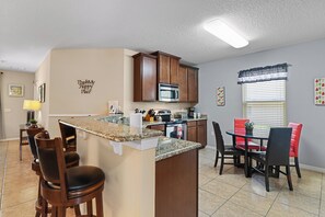 A kitchen with a central island, wooden cabinets, a microwave, and a dining area with red chairs. - Tranquil Terrace - 10 Mins to Disney! (Kissimmee)