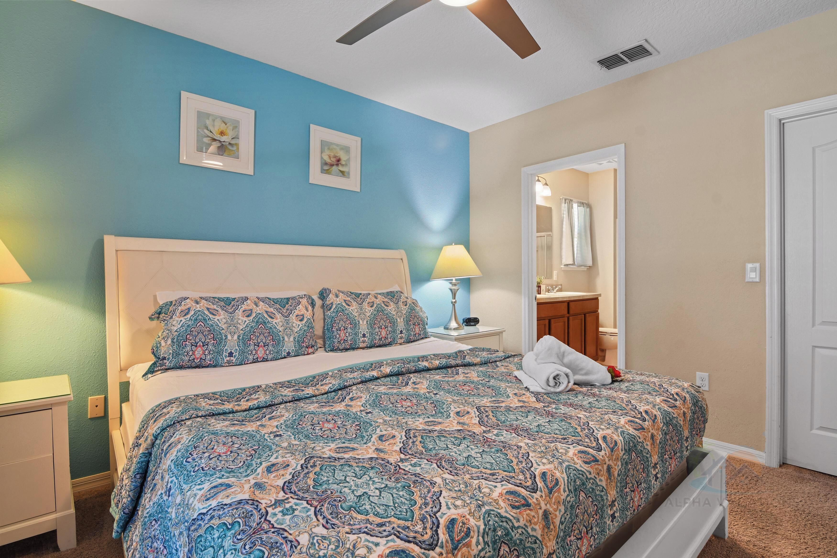 A bedroom with a bed, nightstands, a ceiling fan, and a bathroom visible through an open door.