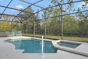 A pool area with a glass enclosure, two lounge chairs, and a hot tub. - Tranquil Terrace - 10 Mins to Disney! (Kissimmee)